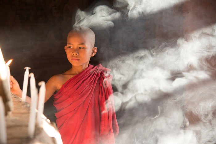 novice monk lights candles and is surround by smoke as he poses for photographers.