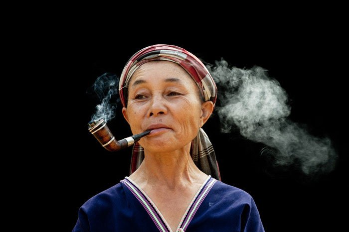 Pwo Karen woman smoking a pipe being photographed in an outdoor natural light portrait studio by Kevin Landwer-Johan