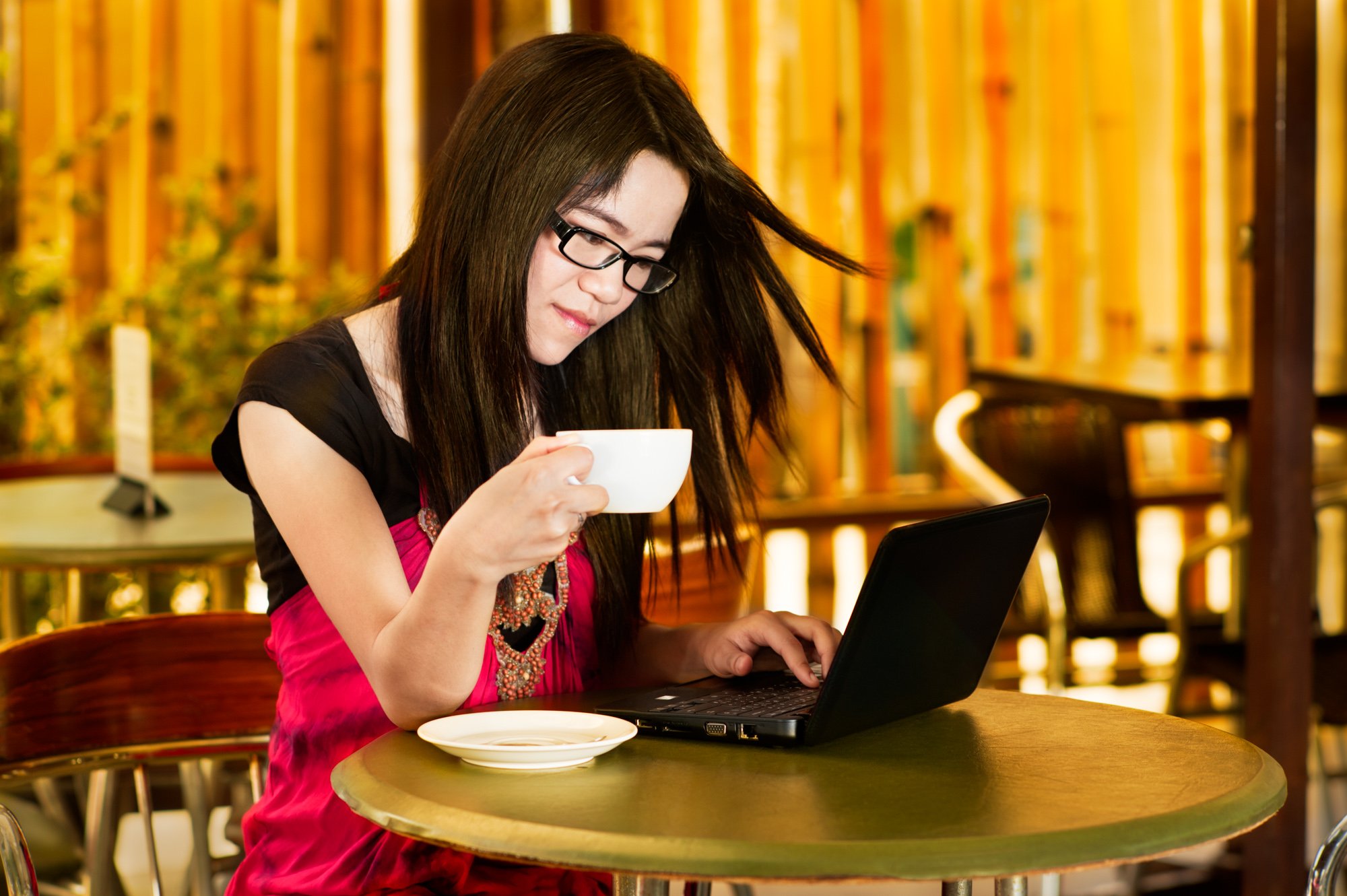 Young Asian woman with a laptop computer drinking coffee at an out door cafe for how to make photo stories