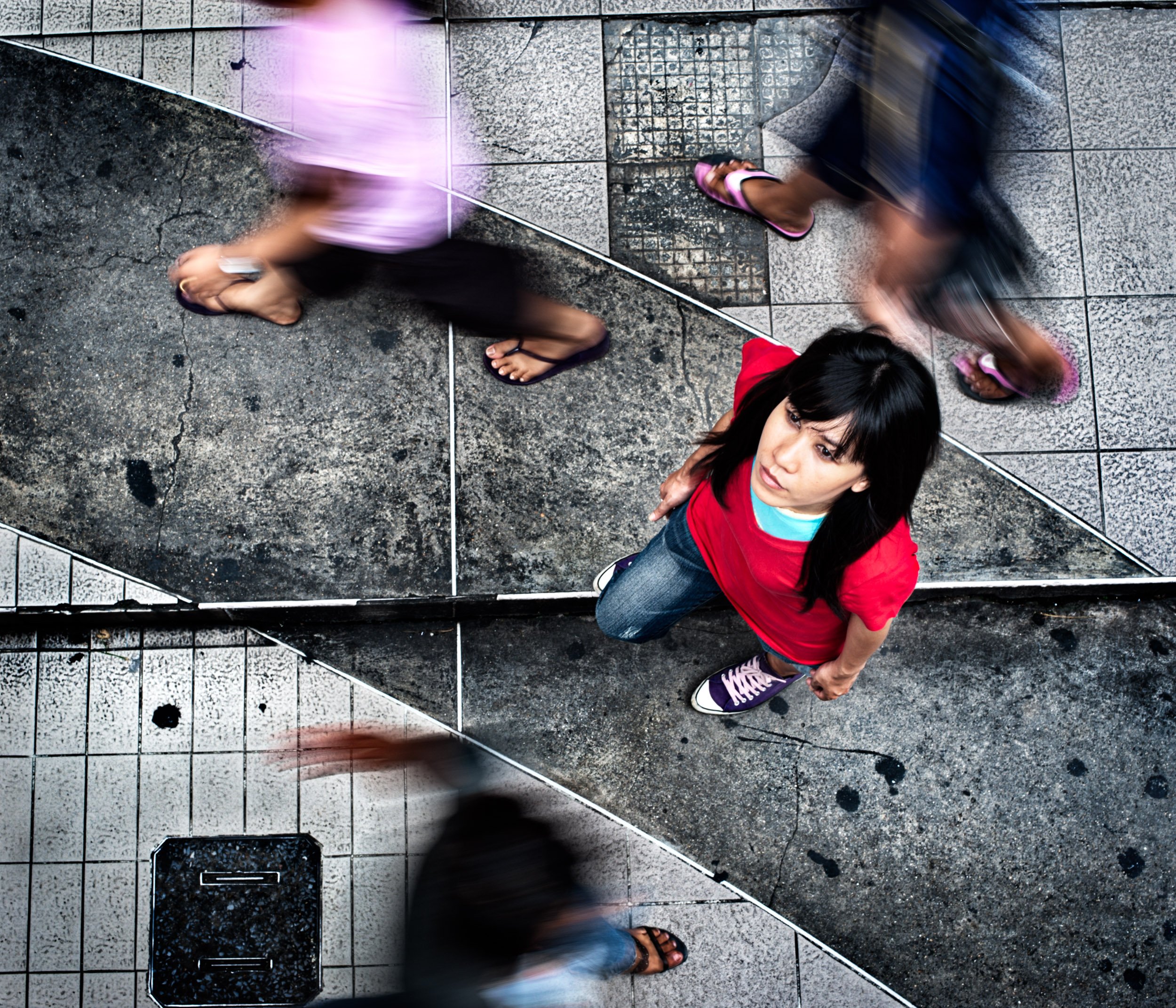 Looking down on an Asian young woman standing on a sidewalk.